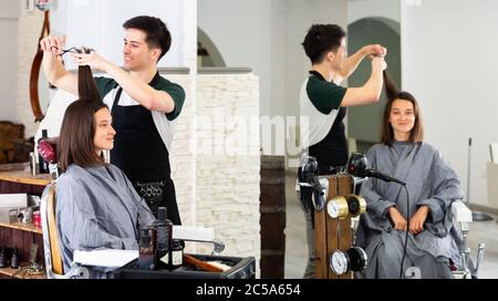 Positive männliche Friseur macht Haar Styling für junge Frau, Arbeitstag im Schönheitssalon Stockfoto