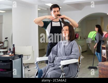 Positive männliche Friseur macht Haar Styling für junge Frau, Arbeitstag im Schönheitssalon Stockfoto