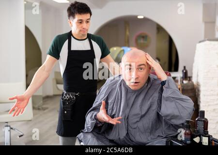 Portrait von wütenden Mann mit rasierten Kopf schockiert von Haarschnitt und bedauern Friseur in modernen Friseursalon Stockfoto