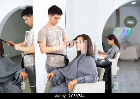 Positive männliche Friseur macht Haar Styling für junge Frau, Arbeitstag im Schönheitssalon Stockfoto