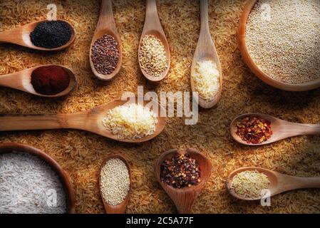 Flaches Stillleben mit braunem Reis, Schüsseln und Löffeln mit verschiedenen Gewürzen, Körnern und Gewürzen. Stockfoto