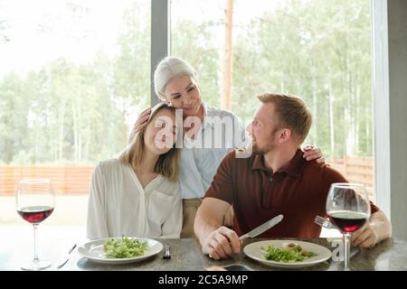 Lächelnd liebende ältere Mutter umarmt Tochter und ihren Mann, während sie sie in Landhaus besuchen Stockfoto