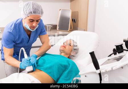 Junge Frau immer fettreduktive Haut Lifting Körperbehandlung auf moderne Geräte in der Kosmetik-Klinik Stockfoto