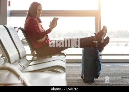 Junge Frau liest Buch wartet auf den Flug am Flughafen Stockfoto