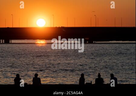 Helsinki / Finnland - 26. JUNI 2020: Silhouetten von glücklichen Menschen, die das Sommerwetter an der Küste während des Sonnenuntergangs genießen. Stockfoto