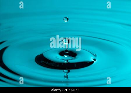 Perfekter Wassertropfen, der in glattes Wasser spritzt und Wellen verursacht Stockfoto