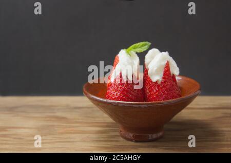 Eine Portion Erdbeeren mit Sahne auf Holztisch und dunklem Hintergrund mit Kopierplatz Stockfoto