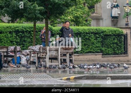 LONDON, ENGLAND - 10. JUNI 2020: Chinesische alte Frau mittleren Alters füttert die Tauben an einem Nieseltag in Holborn, London während der COVID-19 Pandemie 06 Stockfoto