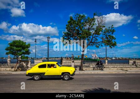 Havanna, Kuba, Juli 2019, ein alter gelber Autofahrpass auf der Malecon eine Fahrstraße entlang der Küste Stockfoto