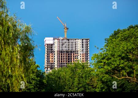 Bau eines mehrstöckigen Gebäudes monolithischen Rahmen mit Schalung gegen einen blauen Himmel und im Vordergrund grüne Parkbäume. Stockfoto