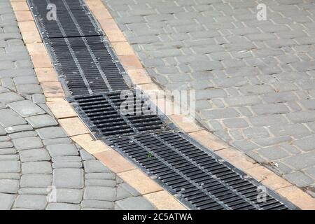 Schwarzes Kühlergrill Entwässerungssystem im Fußgängerweg aus Steinfliesen installiert. Stockfoto