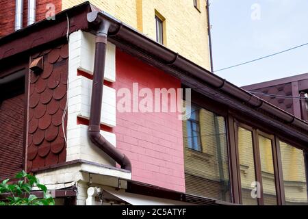 Braune Dachvisier Ablaufrinne auf einer Ziegelwand mit einem Fenster. Stockfoto