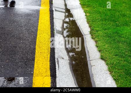 Das aktuelle Regenwasser im gefüllten Kanal ist ein Zementgraben des Abflusssystems auf der Seite einer nassen Asphaltstraße nach Regen, Hintergrund auf der Oberseite Stockfoto