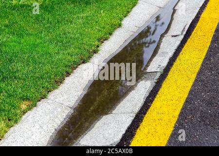 Fließendes Regenwasser im gefüllten Kanal ist ein Zementgraben eines Drainagesystems auf der Seite der nassen Asphaltstraße nach Regen. Stockfoto