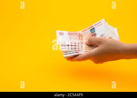 In der Hand ein Pack von fünftausend russischen Rubel, gelber Hintergrund Stockfoto