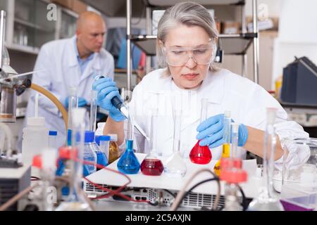 Erfahrene weibliche Biochemiker Mischen von Chemikalien während der genetischen Veränderung Experimente im modernen Labor Stockfoto