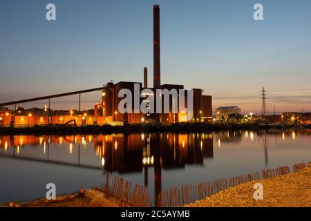 Nächtliches Stadtbild eines Industrieviertels mit einem großen beleuchteten Kraftwerk, das an einem Ufer steht. Stockfoto