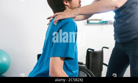 Physiotherapeut, der mit behinderten Menschen im Rollstuhl auf einem Therapietisch trainiert. Stockfoto