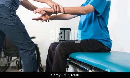 Physiotherapeut, der mit behinderten Menschen im Rollstuhl auf einem Therapietisch trainiert. Stockfoto