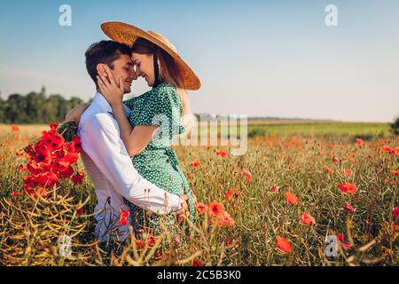 Liebevolles Paar zu Fuß in Mohn Feld mit Blumenstrauß. Glücklich Mann heben Frau Spaß haben. Sommer Stockfoto