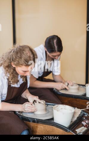 Zwei Keramikkünstlerinnen in Schürze mit Tonmaterial arbeiten im Töpferstudio. Abends freiberufliches Fernstudium. Hobby-Abenteuer für Erwachsene. Winter Stockfoto