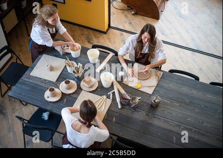 Draufsicht auf weibliche Töpfer während des Arbeitsprozesses in der Tonwerkstatt. Frau Meister bereiten Keramik-und Ton-Produkte an großen Holztisch Stockfoto