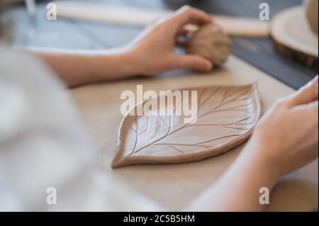 Weibliche Hände halten Stock und machen Ornament auf dekoratives Produkt. Clay Master Formen Ton auf einer Keramik-und Keramik-Werkstatt. Stockfoto