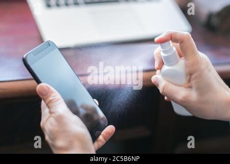 Desinfizieren von Mobiltelefonen mit Alkoholspray Stockfoto