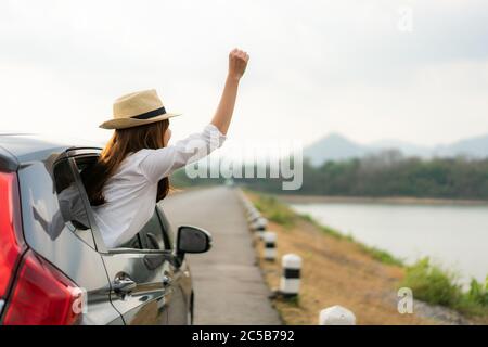 Frau entspannend und genießen Roadtrip. Junge asiatische happines weiblich tragen Hut innen kompakt schwarz Auto mit heben ihre Hand aus dem Auto Fenster mit Stockfoto
