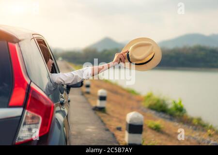 Frau zur Spree Zeit entspannend und genießen Roadtrip. Junge asiatische happines weiblich innen kompakt schwarz Auto mit heben sie Hut aus dem Auto Fenster Witz Stockfoto