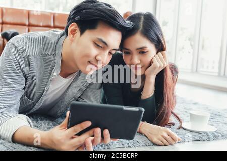 Junges Paar Liebe entspannen Genuss beim Online-Shopping auf elektronischem Tablet im Wohnzimmer, Porträt von asiatischen Paar Entspannung auf einer Couch während Shopp Stockfoto