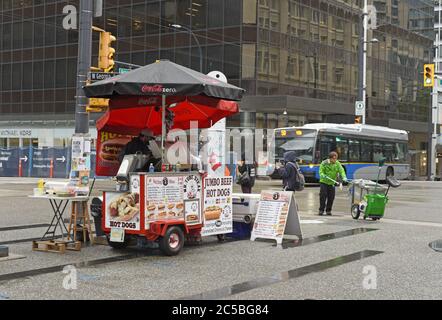 Ein Straßenreiniger arbeitet, als ein Bus hinter einem Hot Dog Food-Händler an der Ecke von Granville Street und W. Georgia Street in der Innenstadt von Vancouver, B Stockfoto