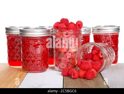 Ganze frische Himbeeren in offenen Maurer Gläser, ein verschüttetes Obst auf dem Tisch vor voll hausgemachten Dosenkonserven Himbeer Konfitüren Gläser auf hellem Holz Tab Stockfoto