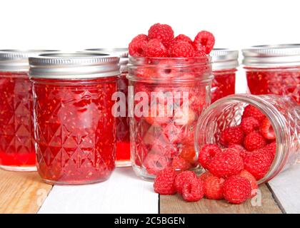 Ganze frische Himbeeren in offenen Maurer Gläser, ein verschüttetes Obst auf dem Tisch vor voll hausgemachten Dosenkonserven Himbeer Konfitüren Gläser auf hellem Holz Tab Stockfoto