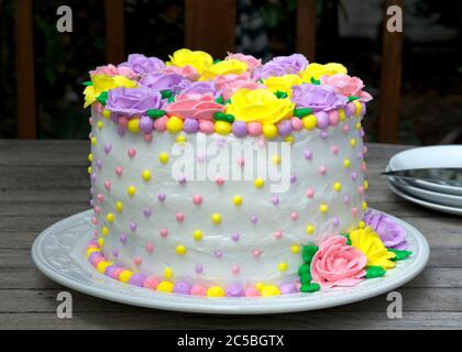 Pastell Regenbogen Gelb, Rosa, Lila Butter Sahne Frosting handgemachte Rosen auf einem runden Kuchen mit weißem Glasur und verziert mit gelb, rosa und Stockfoto