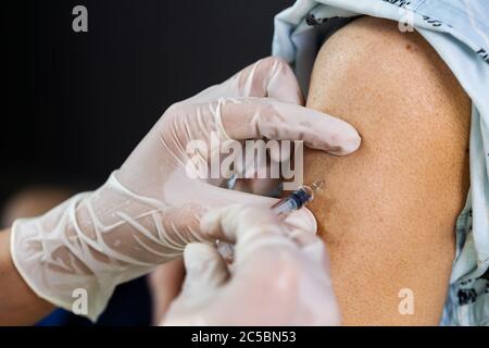 Nahaufnahme Arzt in Handschuhen halten Spritze und macht Injektion zum Patienten. Covid-19 oder Coronavirus-Impfstoff Stockfoto