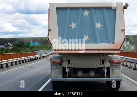 Großer LKW mit der Nationalflagge der Staaten von Mikronesien, der auf der Autobahn vor dem Hintergrund der Dorf- und Waldlandschaft fährt. Stockfoto