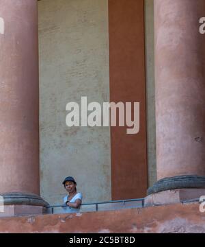 Asiatische Frau in T-Shirt und Hut auf Balkon zwischen großen Säulen in Bologna Italien Stockfoto