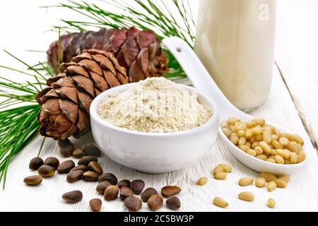 Zedernmehl in einer Schüssel, Nüsse und Zapfen, ein Löffel mit geschälten Nüssen, grünen Kiefernzweig und Zedernmilch in einer Flasche auf Holzbrett Hintergrund Stockfoto