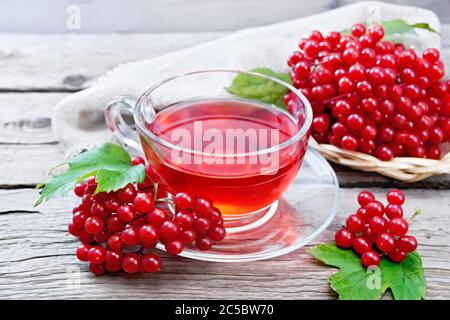 Tee mit Viburnum in einer Glasschale, Weidenplatte mit Beeren, grünen Blättern und Quappe auf dem Hintergrund eines alten Holzbretts Stockfoto