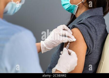 Nahaufnahme Arzt hält Spritze und mit Baumwolle vor Injektion an den Patienten in medizinische Maske. Covid-19 oder Coronavirus-Impfstoff Stockfoto