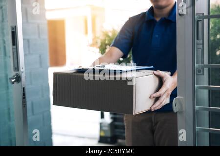 Junger asiatischer Mann lächelt, während sie der Frau einen Karton mit dem Dokument zur Unterschrift liefert. Stockfoto