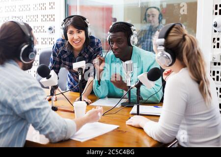 Positive männliche und weibliche Radiomoderatoren diskutieren mit Gästen im Studio Stockfoto