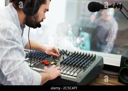 Fokussierter bärtiger Mann, der in der Tontechnik tätig war und bei der Audiosteuerung im Radiostudio arbeitete Stockfoto