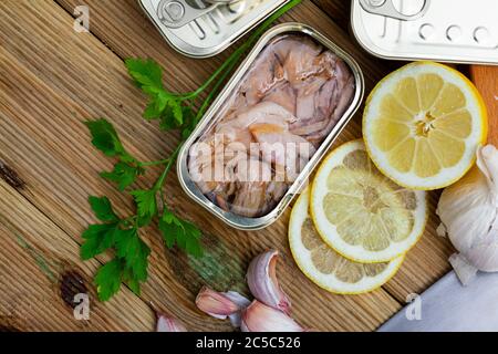 Appetitlich geräucherter Thunfisch Bauchscheiben in Öl in offener Blechdose auf Holztisch mit Grüns und Zitrone. Traditionelle Fischkonserven Stockfoto