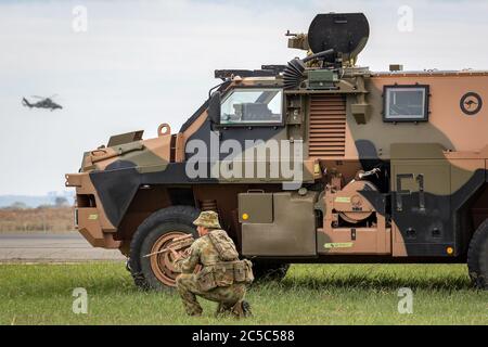 Australischer Soldat mit einem Bushmaster Panzerbewehrungswagen (APC) und einem Army Eurocopter Tiger Hubschrauber. Stockfoto