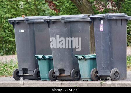 Schwarze Mülltonnen mit nicht recycelbarem Müll, grüne Mülltonnen mit Essensabfällen, die am wöchentlichen Mülltag auf dem Bürgersteig abgestellt wurden. Stockfoto