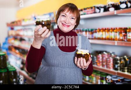 Ältere Kundin hält im Supermarkt Glas mit Marmelade Stockfoto