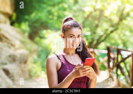Mädchen Athlet vor dem Training wählt Musik auf einem Smartphone. Porträt eines schönen Sportmodels im Park mit einem Telefon in der Hand Stockfoto