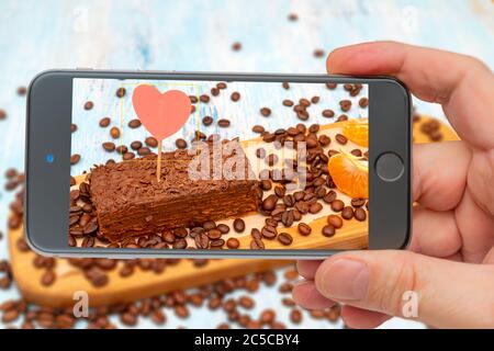 Frischer Schokoladenkuchen. Foto-Smartphone. Smartphone in der Hand. Kuchen im Monitor. Stockfoto